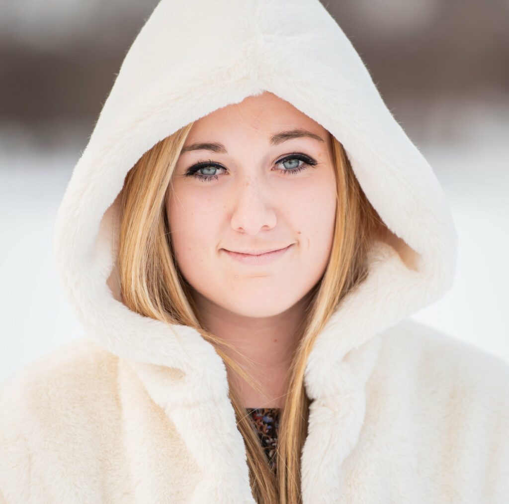 Girl with blue eyes standing in the snow with a fur white coat on