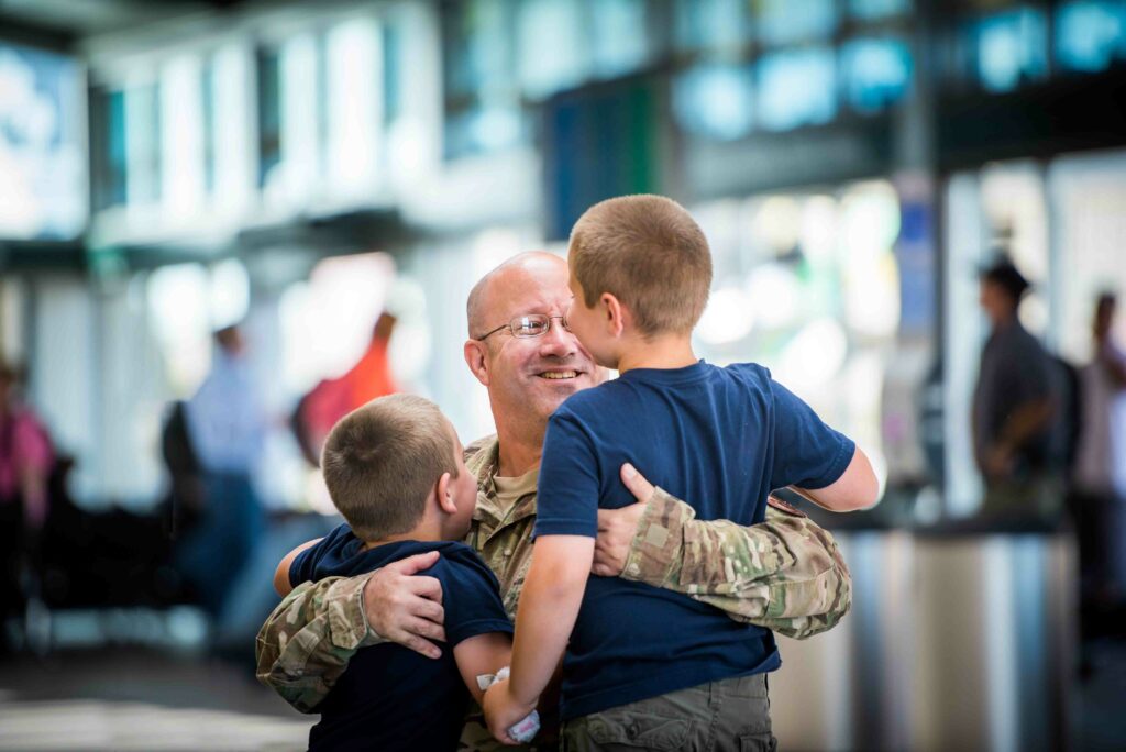 Portrait of a military father returning home from a deployment embracing his two young sons that he hasn't seen in a while.