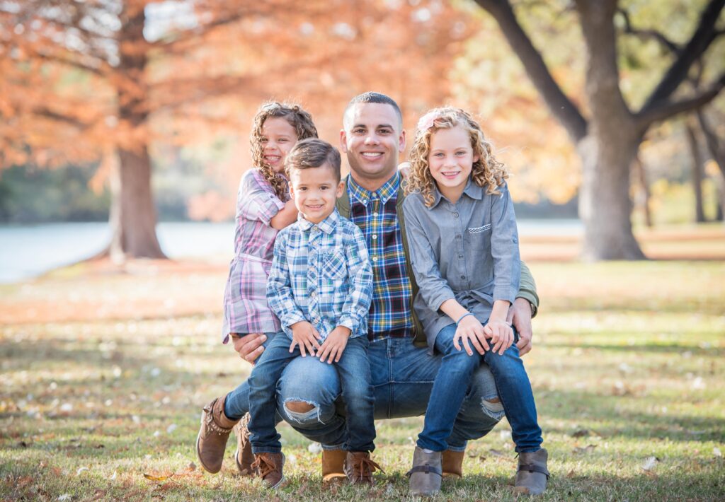 Dad with his three kids in the woods during the fall with beautiful colors on the trees during a family session