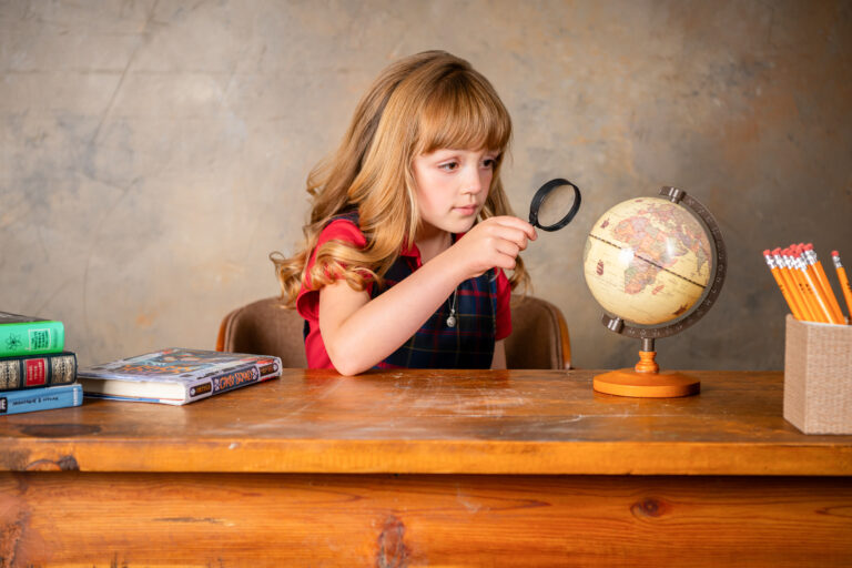 Little Girl looking at a globe with a magnifying glass behind her desk