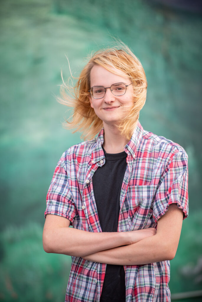 High school senior boy with long hair standing in front of a green wall