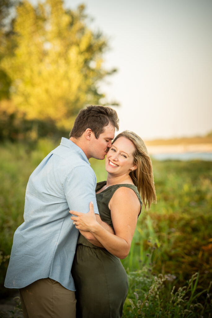 A newly engaged couple kissing and laughing in front of the sunset during an Omaha family session