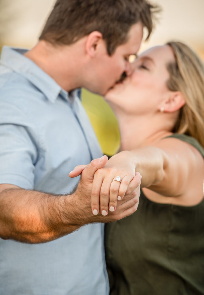 A couple during an engagement session during an Omaha family session kissing and holding out their hands to show the ring