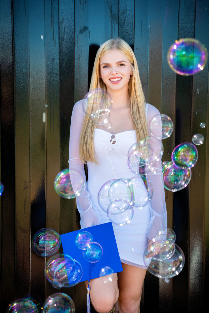 Senior in white dress with graduation cap and bubbles