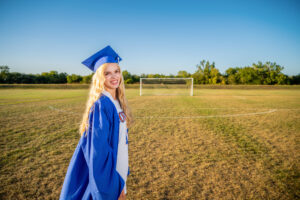 High school at the soccer field in her gap and gown and uniform