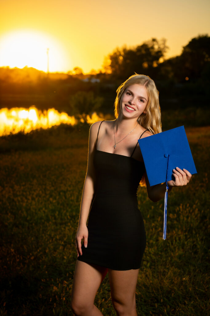 High school senior at sunset holding her cap while in a black dress