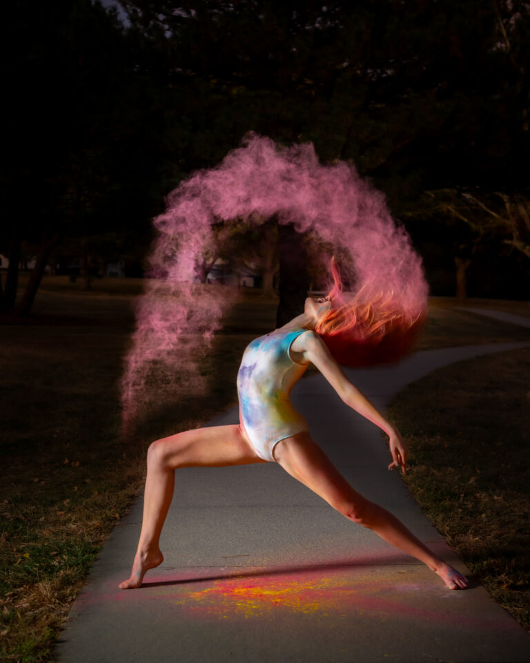 A young dancer outdoors with powder paint in her hair throwing it into the air