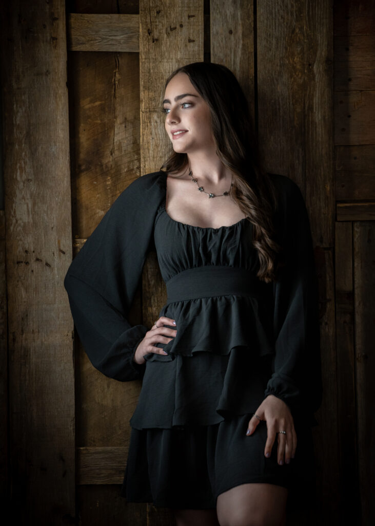 Female high school senior in a black dress and wood background