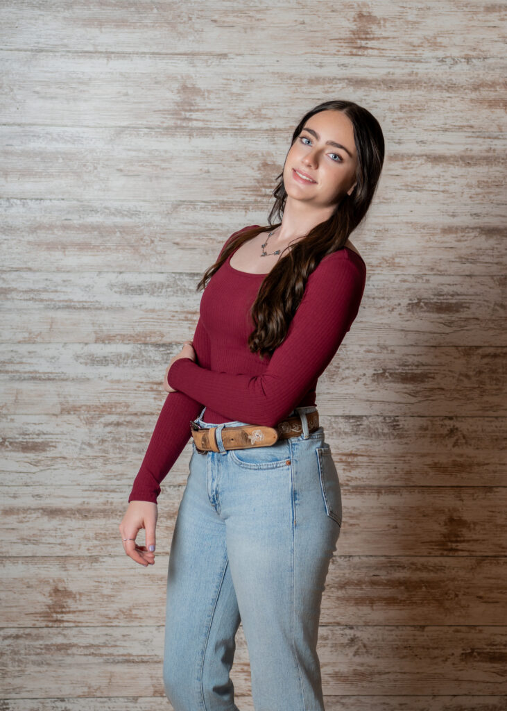 Female high school senior in a red sweater smiling with a light colored wood background