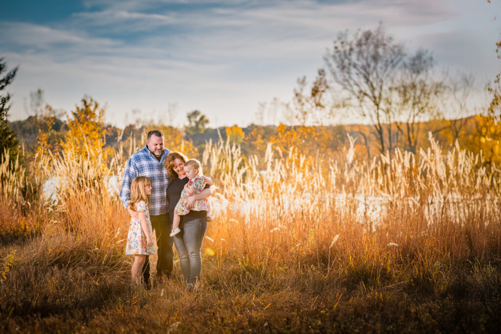 Family of four on a Fall day in the tall grass with the sunset in the background